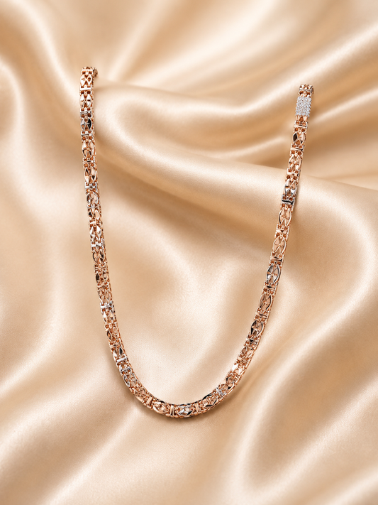 A rose gold tennis necklace with clear gemstones, draped in a U-shape over a beige satin fabric background.