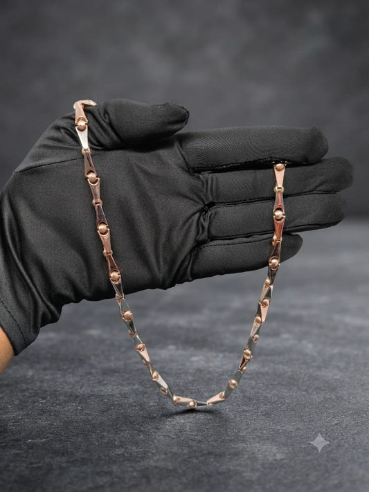 A black satin glove holds a rose gold chain necklace with geometric links against a dark gray textured background.