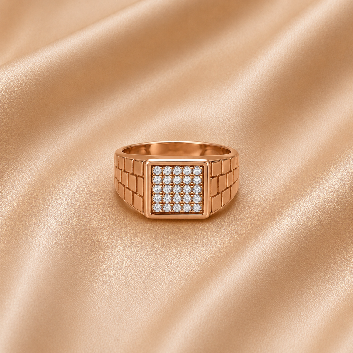 A rose gold signet ring with a square face paved with small clear stones, resting on a draped champagne satin fabric background.