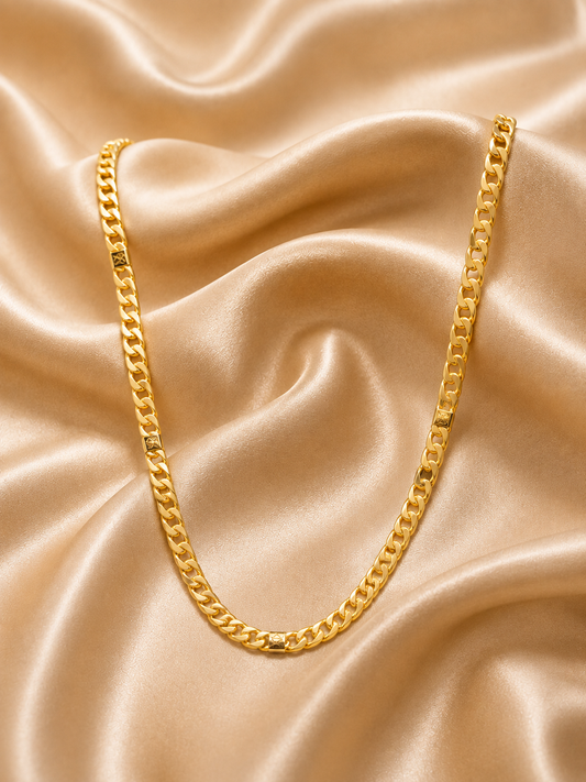 A gold curb chain necklace draped elegantly over draped champagne satin fabric.