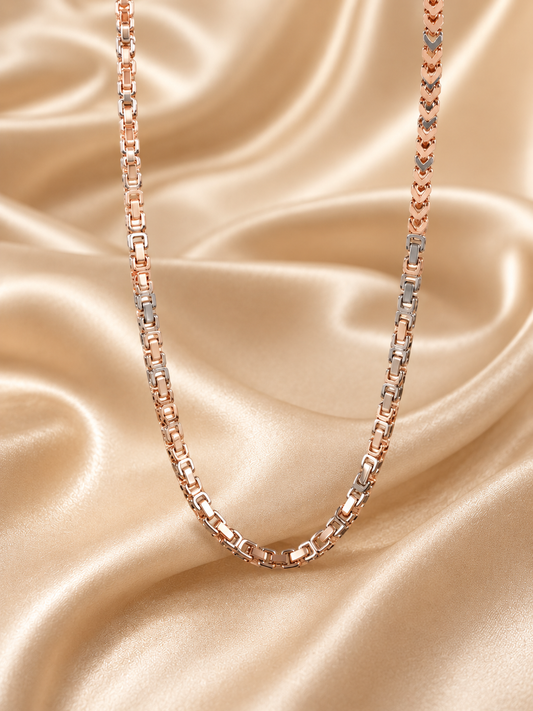 A two-tone chain necklace with rose gold and silver links, draped elegantly over a shimmering champagne satin fabric background.