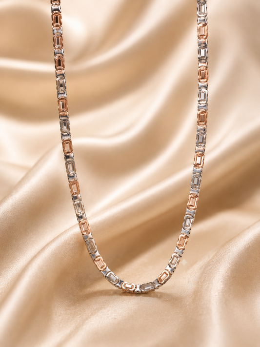 A two-tone chain necklace featuring alternating silver and rose gold rectangular links, draped elegantly on a shimmering champagne satin fabric background.