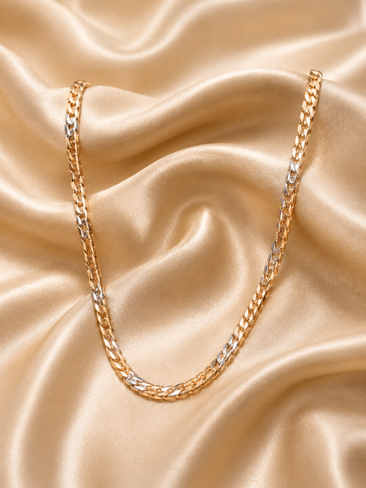 A gold-toned curb chain necklace draped elegantly over draped champagne satin fabric.