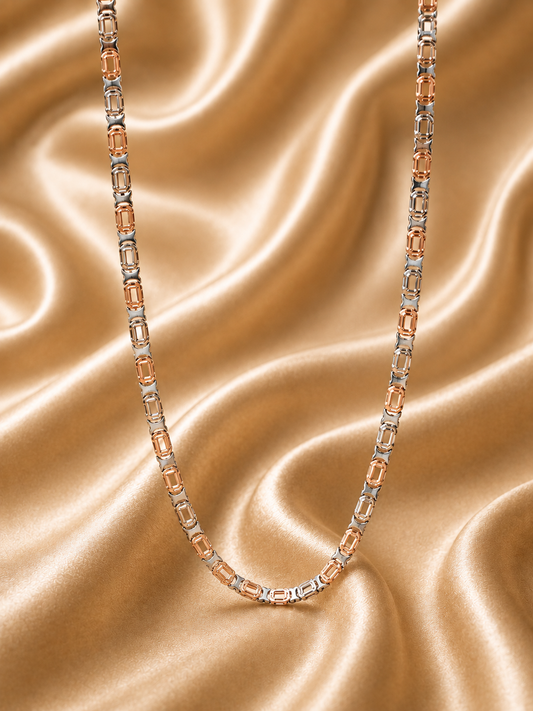 A two-tone chain necklace featuring rose gold and silver-toned metal links, accented with rectangular clear gemstones, displayed on a draped champagne satin fabric background.