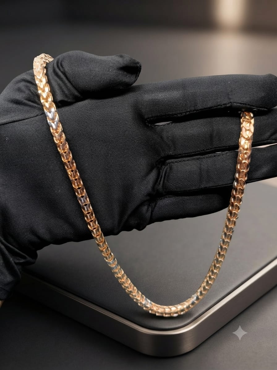 A gold-toned chain necklace draped over a black gloved hand, displayed on a dark surface.