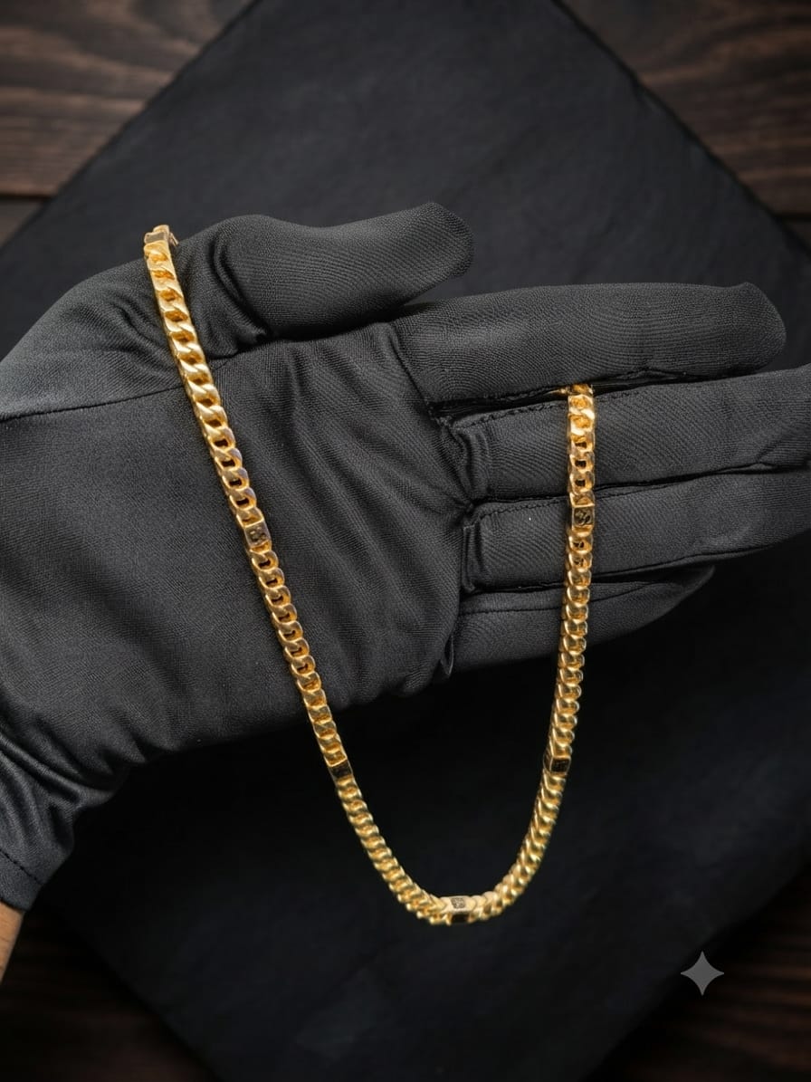 A gold-tone Cuban link chain necklace draped over a black satin-gloved hand, set against a dark textured background.