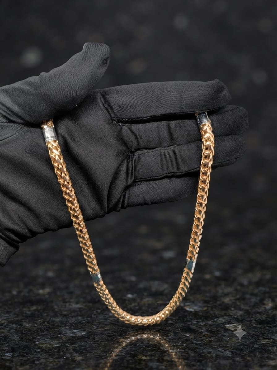 A gold-toned curb chain necklace draped over a black gloved hand, photographed against a dark mottled stone surface.
