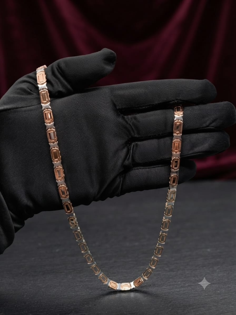 A silver-toned tennis chain necklace with rectangular rose-gold cabochon stones, held by a hand wearing a black glove against a dark red velvet background.