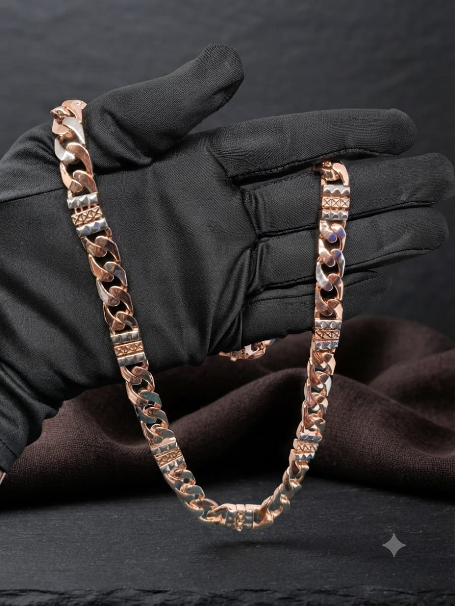 A rose gold Cuban link chain necklace draped over a black satin-gloved hand, set against a dark textured background with draped brown fabric.