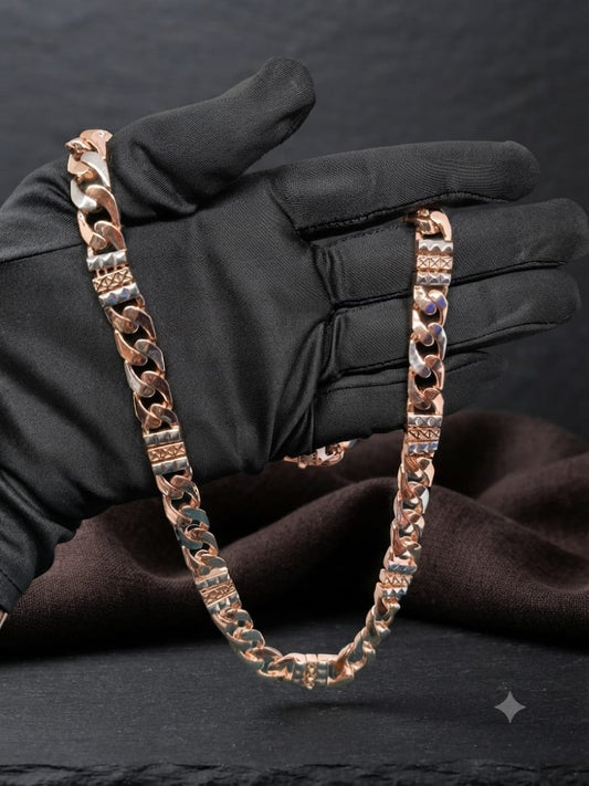 A rose gold Cuban link chain necklace draped over a black satin-gloved hand, set against a dark textured background with draped brown fabric.